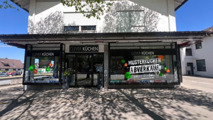 Handgemalte Schaufensterbeschriftung „Musterküchen Abverkauf“ bei Clever Küchen in Gilching mit orange- und grünfarbenen Gestaltungselemente